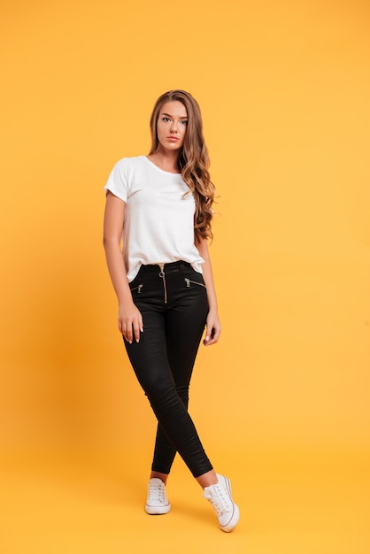Pretty young woman standing and posing isolated over yellow wall