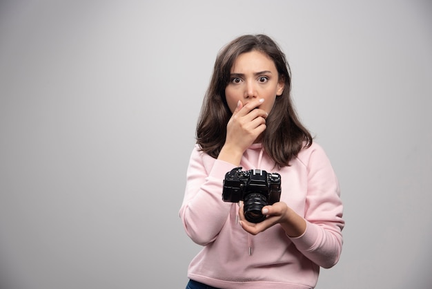 Pretty young woman standing with camera over a gray wall.