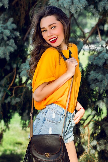 오렌지 셔츠와 boho 가방 세련 된 청바지 반바지를 입고 여름 공원에서 예쁜 젊은 여자.