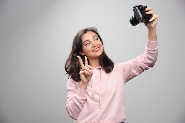 회색 벽에 카메라와 함께 selfie를 복용 꽤 젊은 여자.