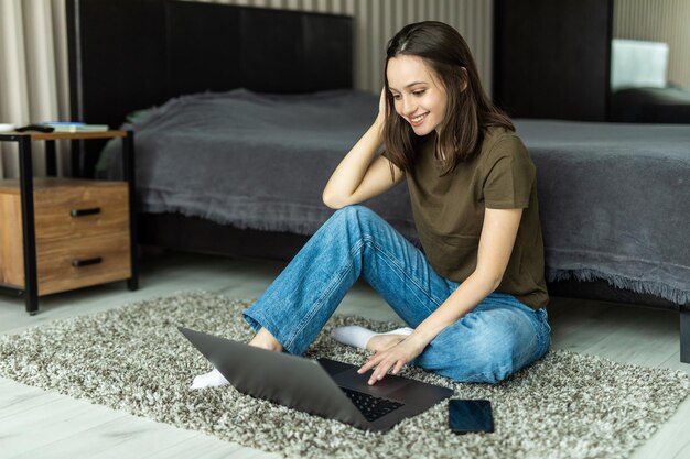 Pretty young woman using her laptop while sitting on the floor at home.