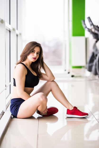 Pretty young woman with big green eyes strong fit body long brown hair is posing in gym in front of the windows