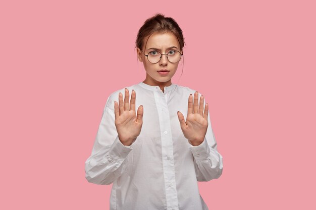 Pretty young woman with glasses posing against the pink wall