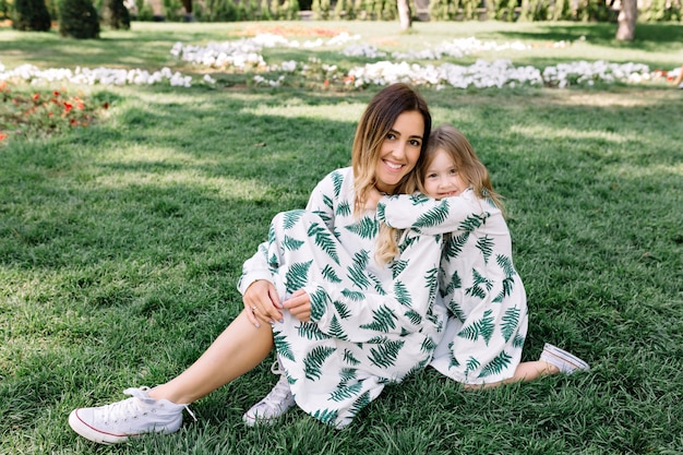 Foto gratuita la giovane donna graziosa con la piccola figlia è seduta sull'erba alla luce del sole