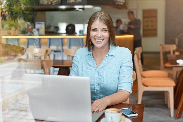 Pretty young woman with long hair sitting in cafe with laptop