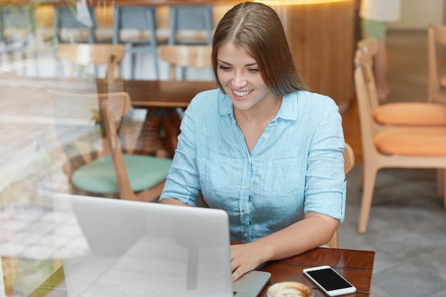 Pretty young woman with long hair sitting in cafe with laptop