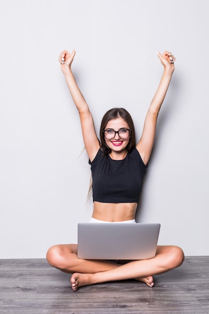 Pretty young woman with modern laptop sitting near grey background