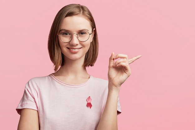 Pretty young woman with round glasses and ribbon for breast cancer awareness