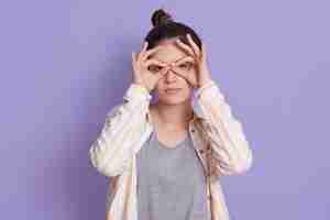 Free photo pretty young woman with upset face holding fingers near eyes like glasses