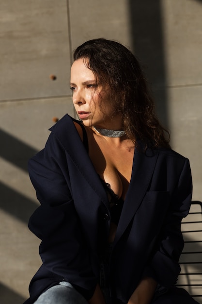 Pretty young woman with wet hair posing in studio, wearing black oversize blazer and shiny necklace