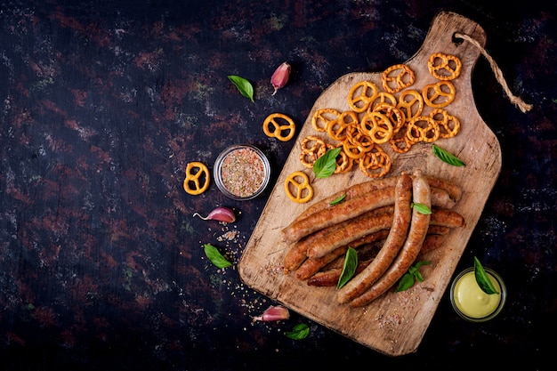 Pretzels and grilled sausages on dark background. Oktoberfest. Flat lay. Top view