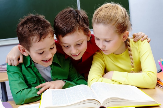 Primary students reading a yellow book with blackboard background