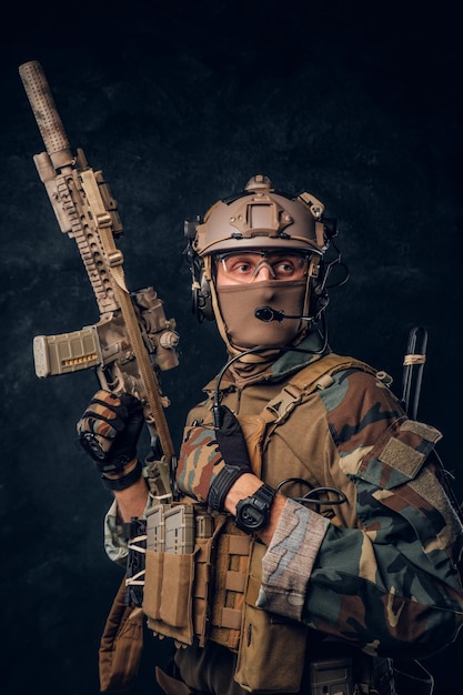 Free photo private security service contractor in camouflage uniform posing with assault rifle. studio photo against a dark textured wall