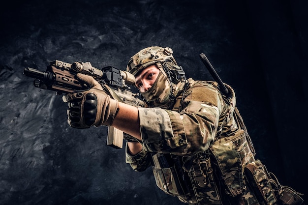Private security service contractors, the elite special unit, full protective soldier holding assault rifle aiming at the target. Studio photo against a dark wall.