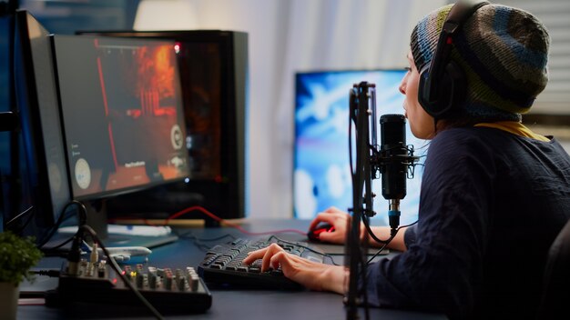 Pro cyber woman talking at streaming professional microphone in gaming home studio with open stream chat. Gamer performing in online tournament using powerful personal computer with RGB and headset