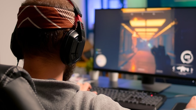 Pro gamer playing on powerful computer first person shooter video game during live championship, wearing headphones. Competitive player streaming video game tournament using professional equipment