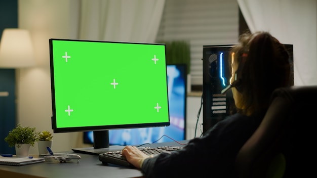Профессиональный геймер, играющий в виртуальную видеоигру на мощном компьютере с макетом зеленого экрана и дисплеем с цветным ключом. Кибер-игрок, использующий профессиональный компьютер с изолированными настольными потоковыми играми-шутерами в головном уборе