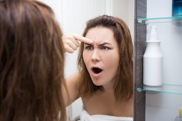問題​の​ある​肌​の​概念​-​バス​ルーム​で​鏡​を​見ている​若い​女性