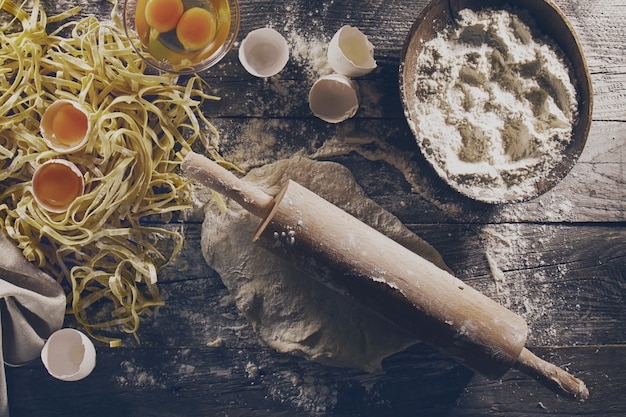 古典的なイタリア料理のための生の新鮮な材料でパスタを調理するプロセス - 生の卵、木製テーブルの小麦粉。上面図。トーニング