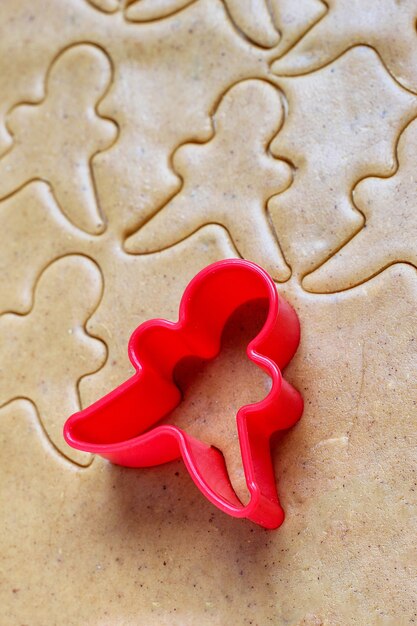 Process of dealing with gingerbread man cookies, use red gingerbread man mold cutting gingerbread dough on baking paper around colorful cookie cutters on white wooden table. top view