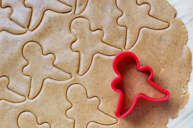 Process of dealing with gingerbread man cookies, use red gingerbread man mold cutting gingerbread dough on baking paper around colorful cookie cutters on white wooden table. top view
