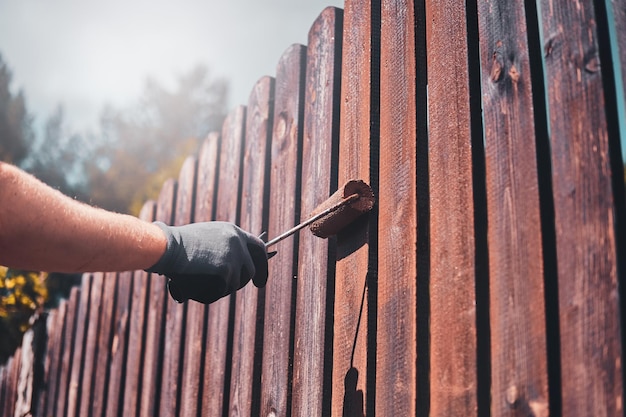 Process of fence renovation at bright sunny day by man in protective gloves.