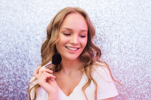 Process of making makeup. Make-up artist working with brush on model face. Portrait of young blonde woman in beauty saloon interior. Applying tone to skin.