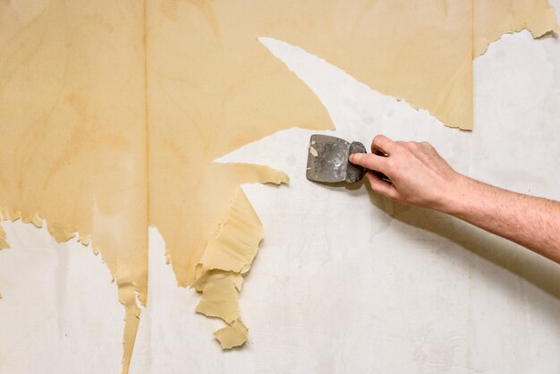 古い壁紙を削除するプロセス 金属ヘラで濡れた古い壁紙から壁を掃除します プレミアム写真