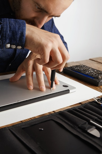 Professional accurately unscrewing case of metallic slim laptop in his electric service lab near tool bag to clean and repair it