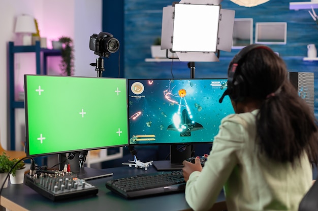 Professional african e sports player streams championship using computer with chroma key. Gamer using pc with greenscreen isolated desktop streaming space shooter video games.