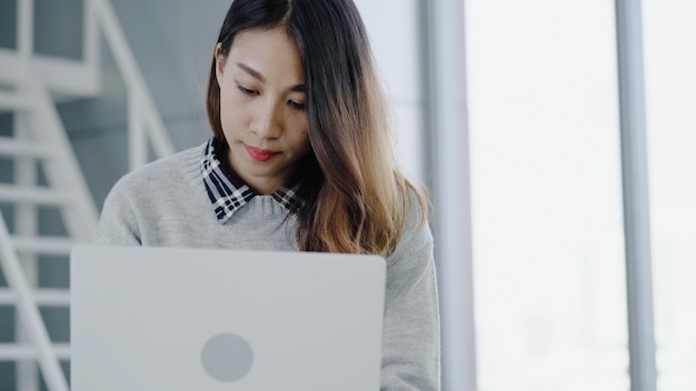 Professional Asian businesswoman working at her office via laptop. Young Asian female manager using portable computer device while sitting at modern workplace.