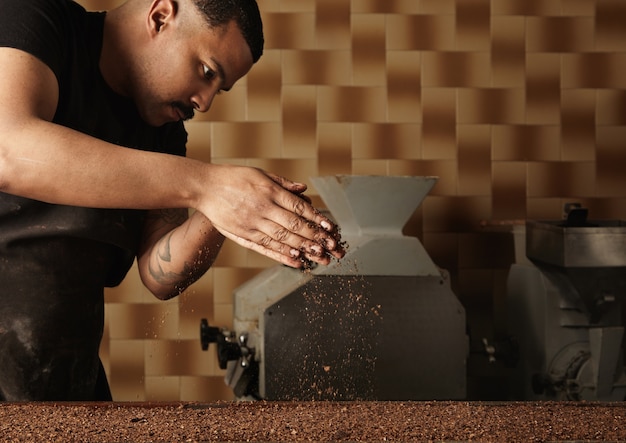 Professional baker pours grained nuts on mold filled with melted chocolate mass. Preparation of tasty cake from organic chocolate in artisan confectionery for sale