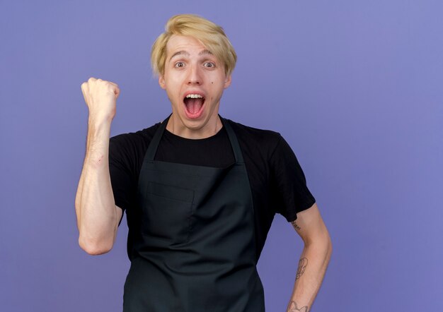 Professional barber man in apron clenching fist happy and excited 