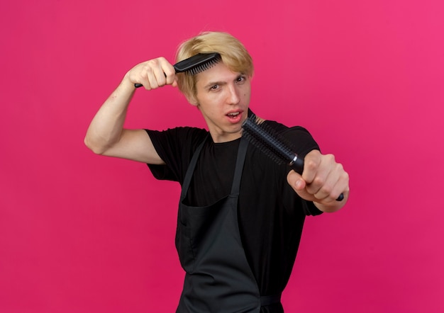 Professional barber man in apron holding hair brushes smiling confident 