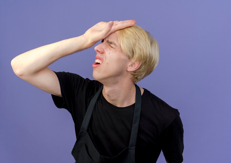 Free Photo professional barber man in apron holding hand on his head being confused 