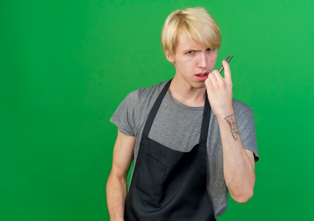 Professional barber man in apron holding razor with serious face 