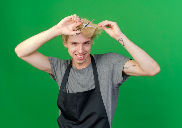 Professional barber man in apron holding scissors cutting his hair smiling 