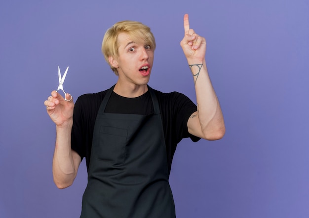 Профессиональный парикмахер в фартуке с ножницами показывает указательный палец с новым выражением идеи