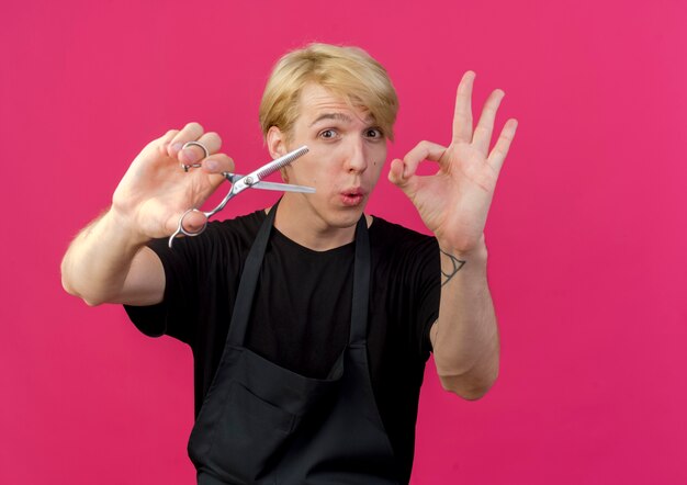 Professional barber man in apron holding scissors smiling showing ok sign 