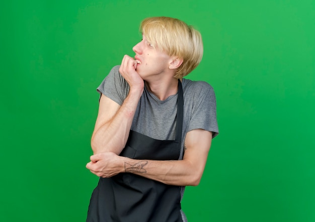 Professional barber man in apron looking aside stressed and nervous 