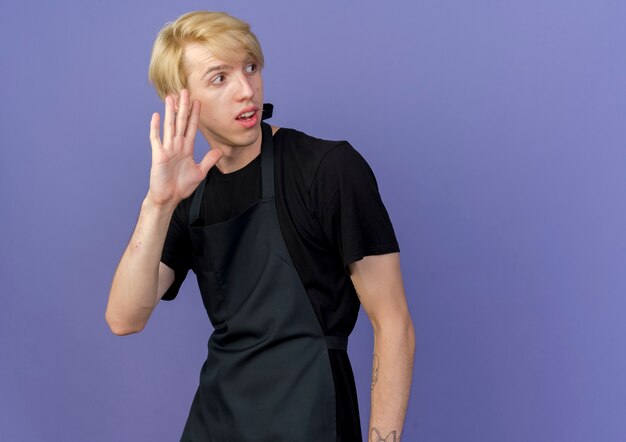 Professional barber man in apron looking aside waving wit hand 