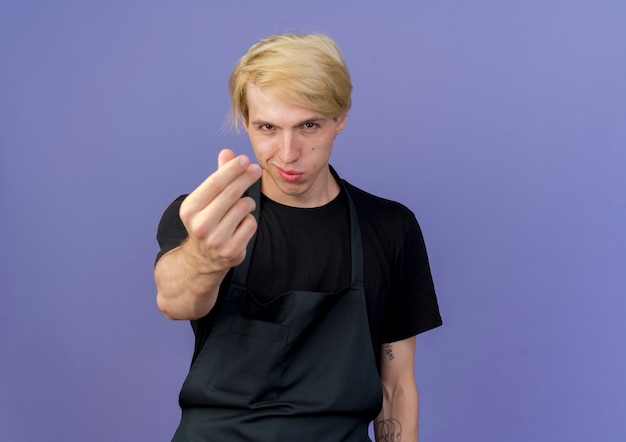 Professional barber man in apron making money gesture rubbing fingers 