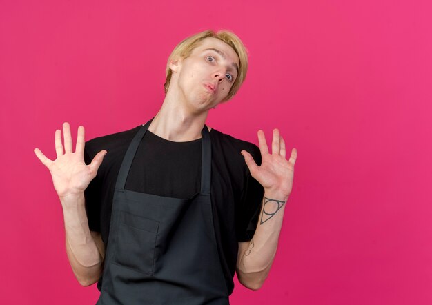 Free photo professional barber man in apron raising hands in surrender