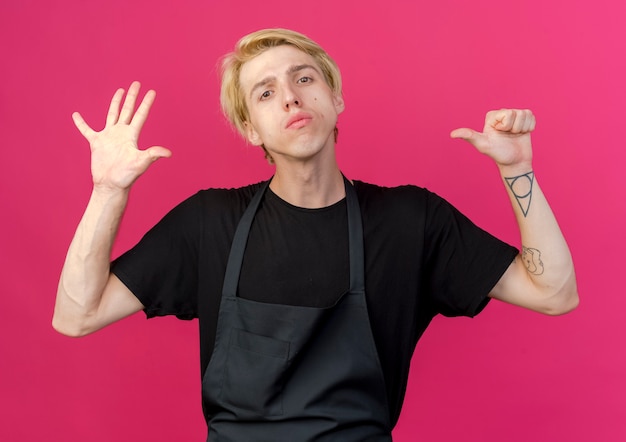 Professional barber man in apron showing number six with serious face 