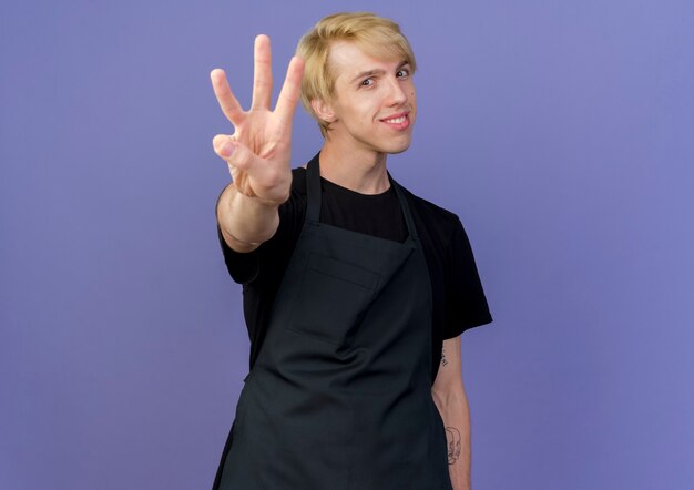 Professional barber man in apron showing and pointing up with fingers number three 