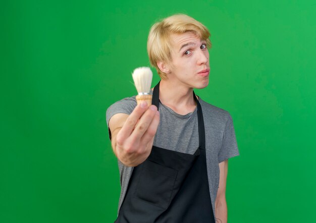 Professional barber man in apron showing shaving brush looking confident 