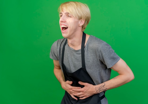 Free photo professional barber man in apron touching his belly laughing out