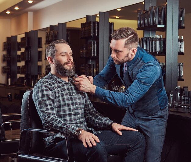 Professional barber working with a client in a hairdressing salon. Styling beard with a trimmer.