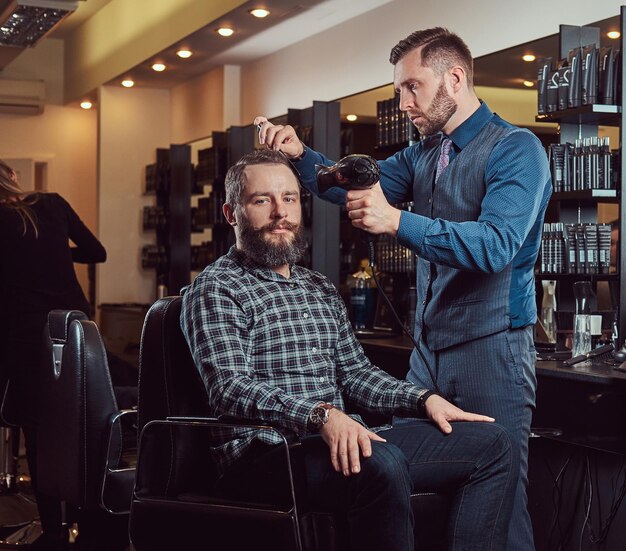 Professional barber working with a client in a hairdressing salon, uses a hair dryer. Men's haircut in a barbershop.