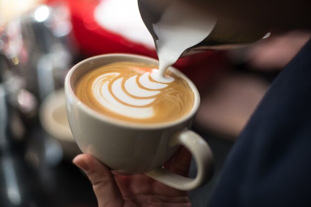 Professional barista pouring milk into the cup of coffee